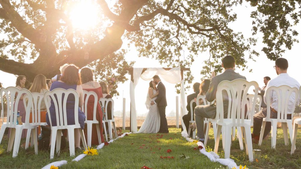 Couples kisses under an oak tree at sunset in a backyard wedding ceremony sonoma county