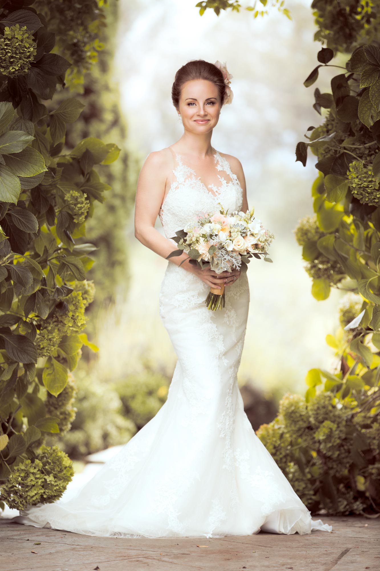 Wedding portrait of a bride in her dress holding a bouquet in a garden