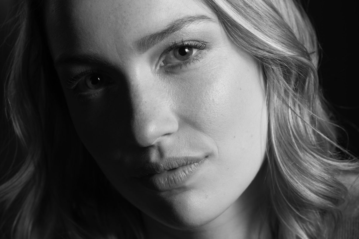 A black-and-white close-up portrait of a woman captures a powerful sense of presence and emotion. Her face fills the frame, angled slightly and softly illuminated to reveal fine details of her skin texture, eyelashes, and subtle expression. Her light hair falls in loose waves, framing her face and catching faint highlights, while the shadows add depth and contrast to her features. The intensity of her gaze, directed just off-camera, conveys quiet strength and introspection. The lack of color enhances the timeless quality of the image, emphasizing form, tone, and expression—hallmarks of a skilled Napa Valley portrait photographer.
